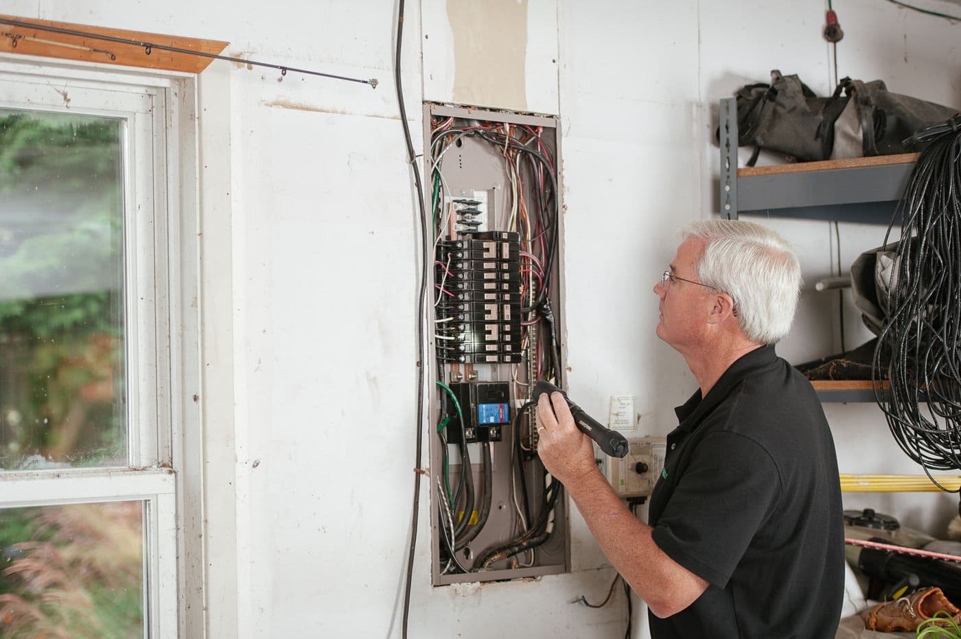 A master electrician testing an open service panel with a voltage tester