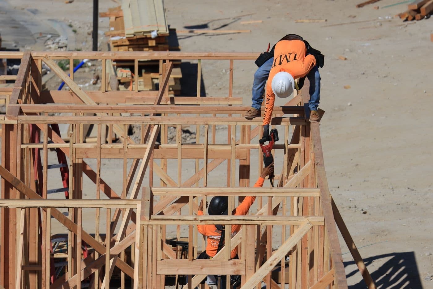 Two carpenters framing a wall on a job site, working from the top plate